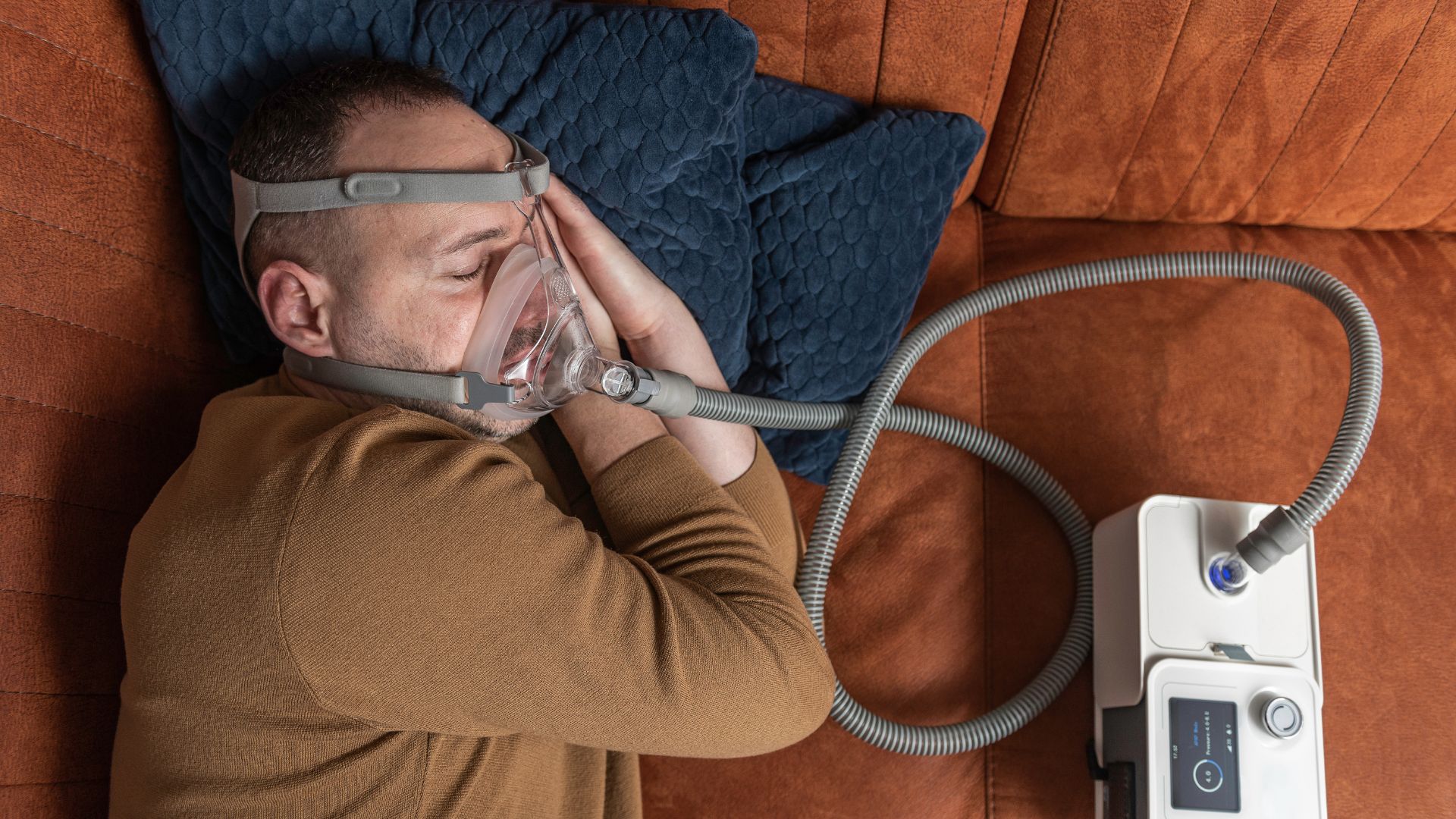 Persona dormida en casa usando CPAP con mascarilla facial completa conectada al equipo